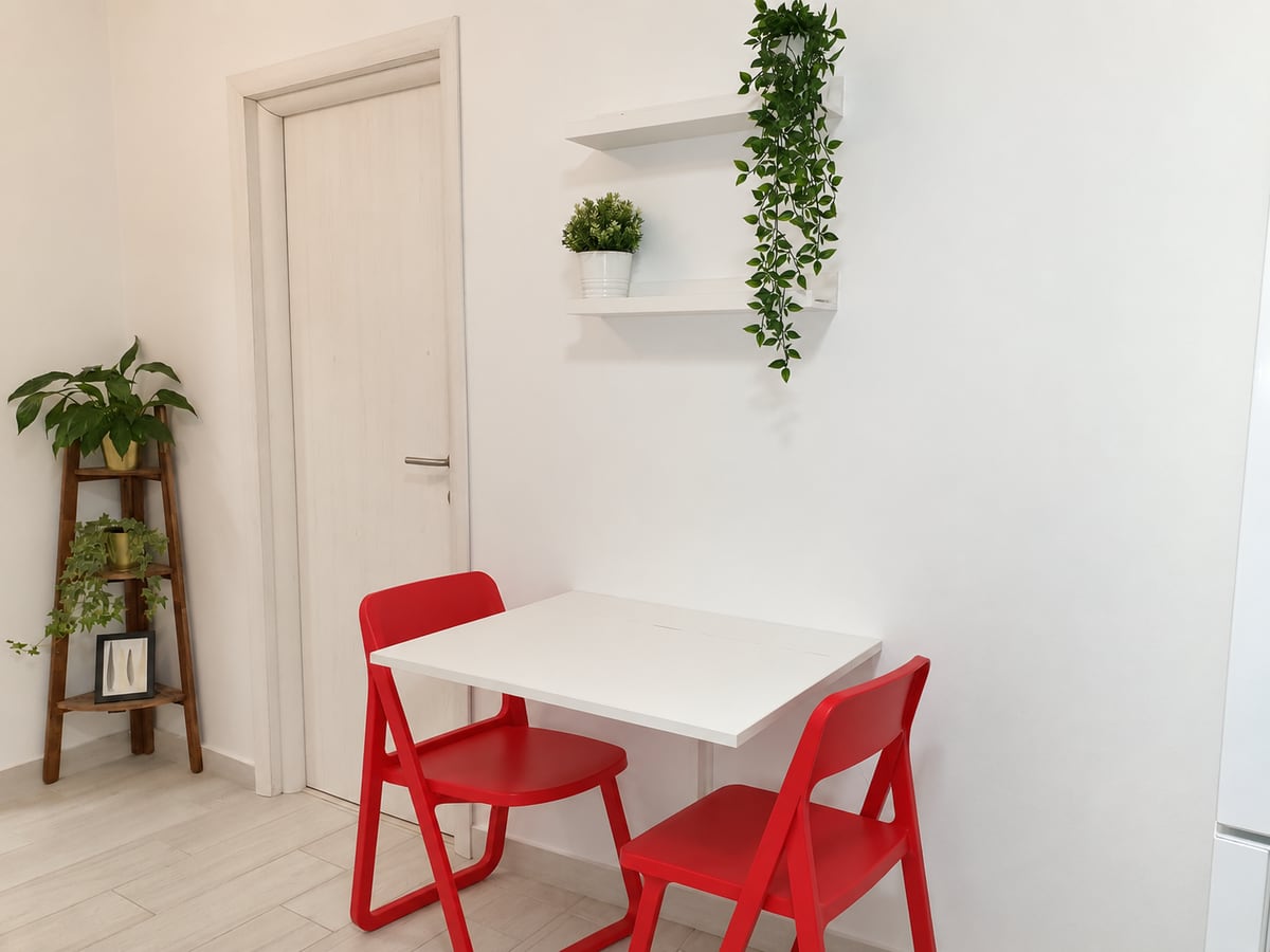The eating area by the entrance: a white folding table with two red folding chairs, a plant ladder and shelves of greenery.