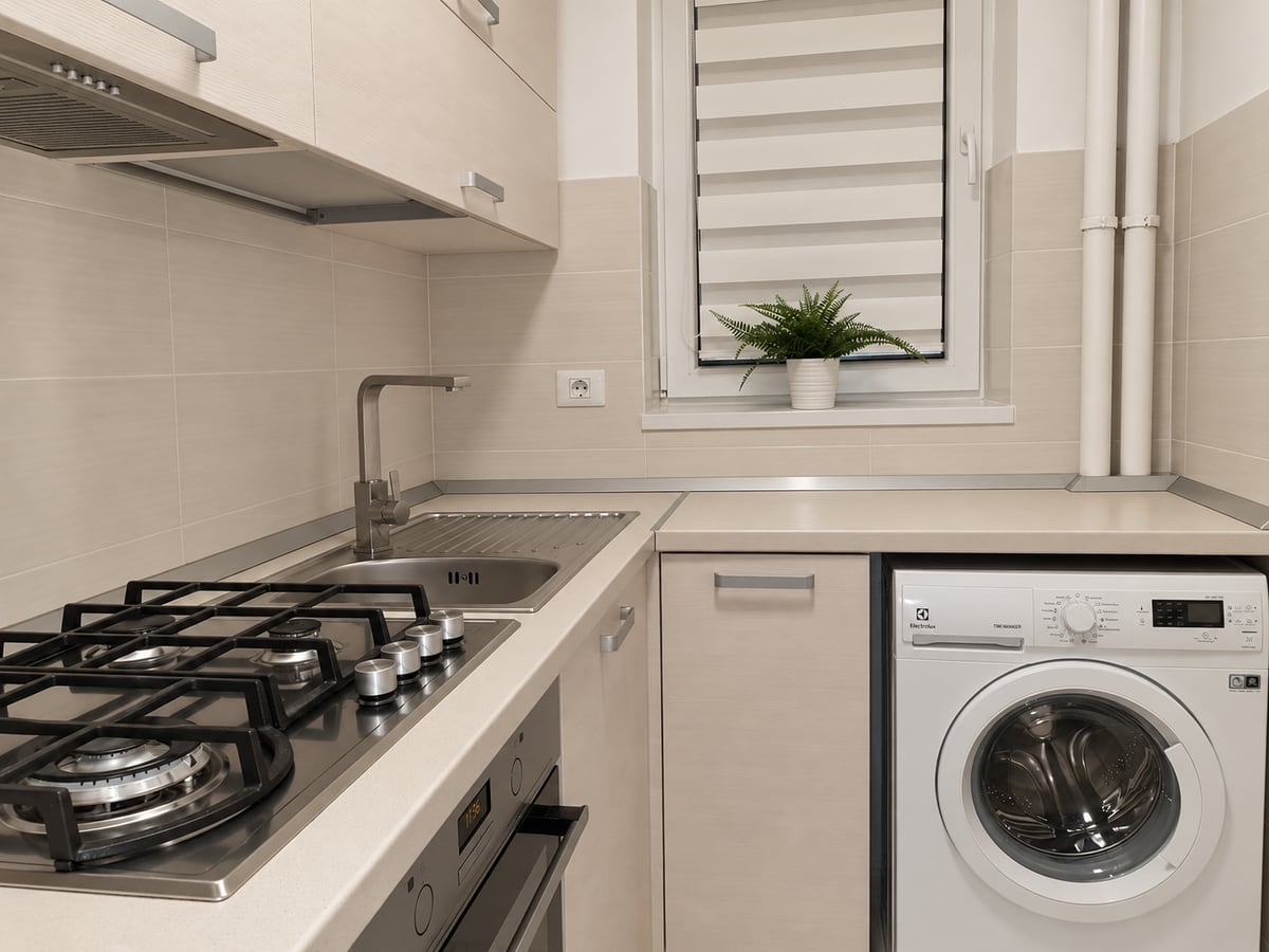 The kitchen from the other side: gas hob and oven, the washing machine built in under the counter and a planted window.