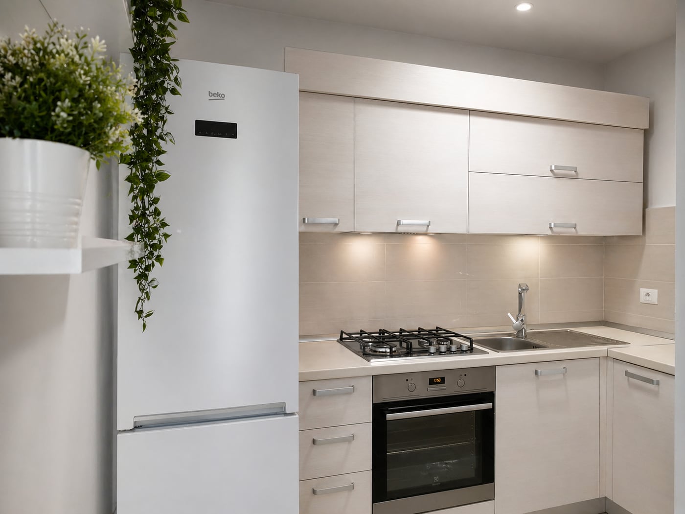 The finished kitchen: pale units built out, gas hob and integrated oven, the fridge behind a shelf of trailing greenery.